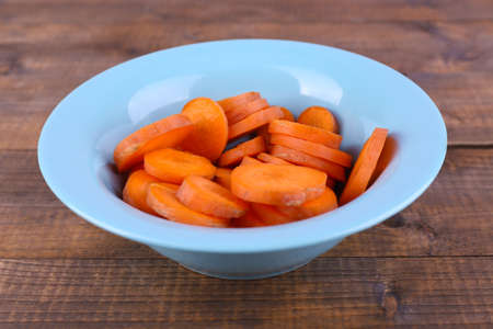 Slices of carrot in blue round bowl on wooden backgroundの写真素材