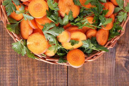 Slices of carrot and parsley in wicker bowl on wooden backgroundの写真素材