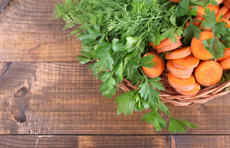 Slices of carrot and parsley in wicker bowl on wooden backgroundの写真素材