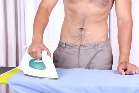 Young man ironing clothes in roomの写真素材