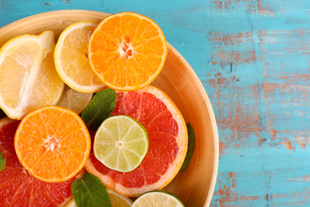 Different sliced juicy citrus fruits in bowl on blue wooden table