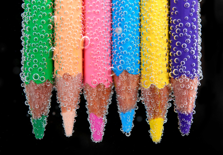 Colorful pencils in water with bubbles on black background