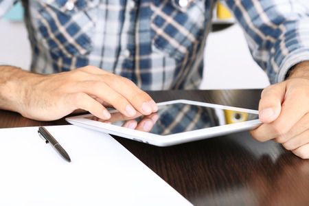 Man sitting on wooden table and working on tablet closeupの写真素材