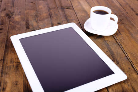 Tablet and cup of coffee on brown wooden backgroundの写真素材
