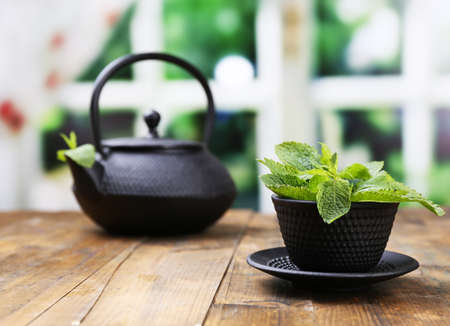 Chinese traditional teapot with fresh mint leaves on wooden table, on bright backgroundの写真素材