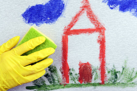 Hand in glove wiping children drawing on wallpaper