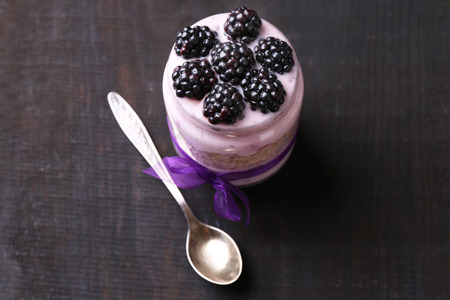 Healthy breakfast - yogurt with  blackberries and muesli served in glass jar, on dark wooden backgroundの写真素材