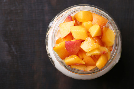 Healthy breakfast - yogurt with  fresh peach and muesli served in glass jar, on wooden backgroundの写真素材