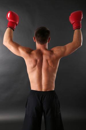 Handsome young muscular sportsman with boxing gloves on dark backgroundの写真素材
