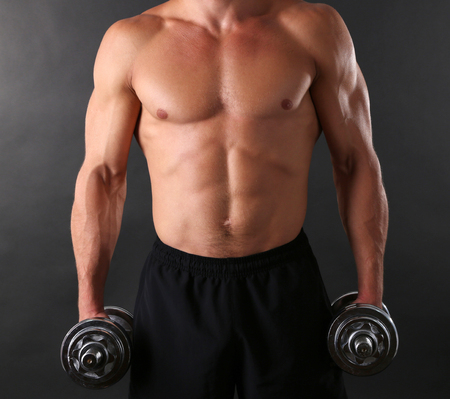 Handsome young muscular sportsman execute exercise with dumbbells on dark backgroundの写真素材