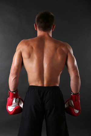 Handsome young muscular sportsman with boxing gloves on dark backgroundの写真素材