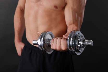 Muscle young sportsman execute exercise with dumbbell on dark backgroundの写真素材