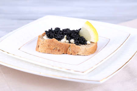 Slice of bread with butter, black caviar and lemon on plate on grey backgroundの写真素材