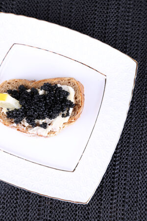 Slice of bread with butter and black caviar on square plate on dark fabric backgroundの写真素材