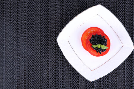 Slices of tomato with black caviar on plate on dark fabric backgroundの写真素材