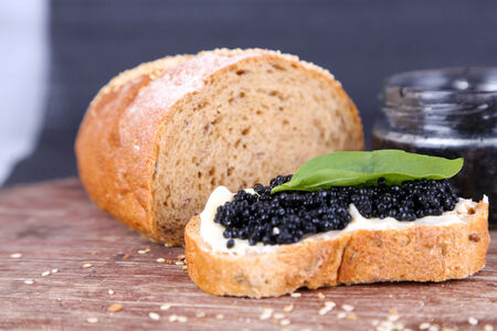 Slices of bread with butter and black caviar on wooden table on dark backgroundの写真素材