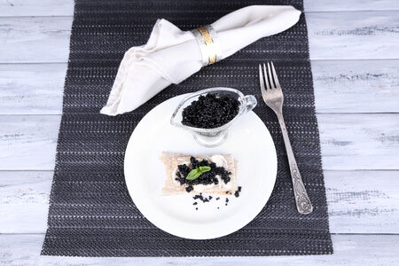 Slice of bread with butter and black caviar on plate on napkin on wooden backgroundの写真素材
