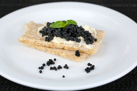 Slices of bread with butter and black caviar on plate on dark fabric background closeupの写真素材