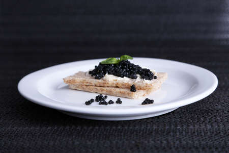 Slices of bread with butter and black caviar on plate on dark fabric backgroundの写真素材