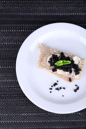 Slices of bread with butter and black caviar on plate on dark fabric backgroundの写真素材