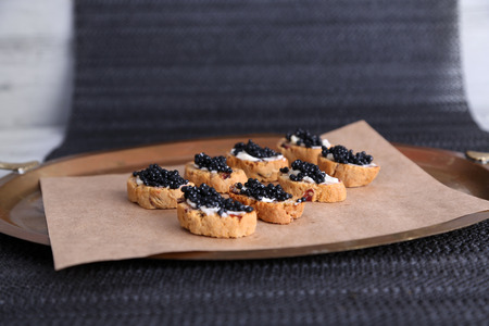 Slices of bread with butter and black caviar on paper on tray on fabric backgroundの写真素材