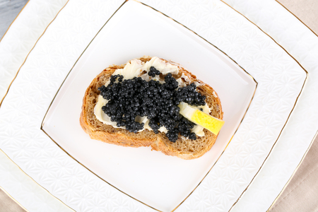 Slice of bread with butter, black caviar and lemon on plateの写真素材