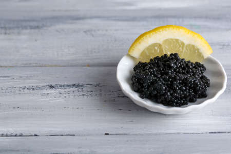 Black caviar with lemon on plate on grey wooden backgroundの写真素材