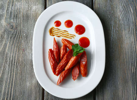 Smoked thin sausages and vegetables on plate, on wooden backgroundの写真素材