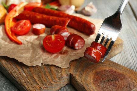 Smoked thin sausages and vegetables on cutting board, on wooden backgroundの写真素材