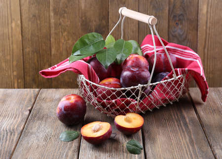 Sweet plums in wicker basket on wooden backgroundの写真素材