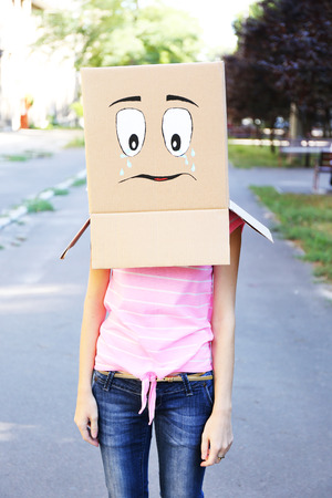 Woman with cardboard box on her head with sad face, outdoorsの写真素材