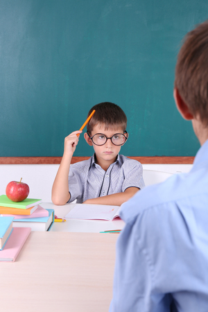 Schoolboy and teacher sitting in classroom on blackboard backgroundの写真素材