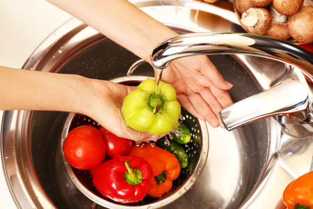 Woman's hands washing vegetables in sink in kitchenの写真素材