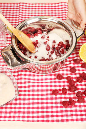 Red raspberries in metal pan and sugar on fabric background