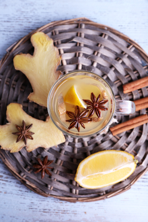 Cup of ginger drink with lemon on wicker mat on wooden backgroundの写真素材