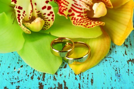 Wedding rings and orchid flowers, close-up, on color wooden backgroundの写真素材