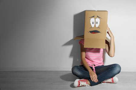 Woman with cardboard box on her head with sad face, near wallの写真素材