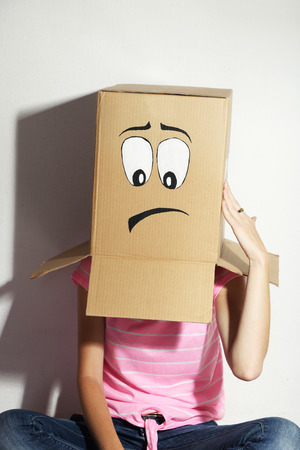 Woman with cardboard box on her head with sad face, near wallの写真素材