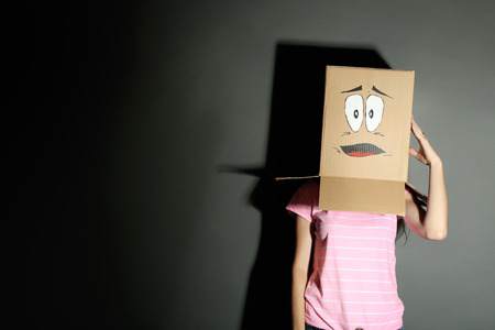 Woman with cardboard box on her head with sad face, on grey background