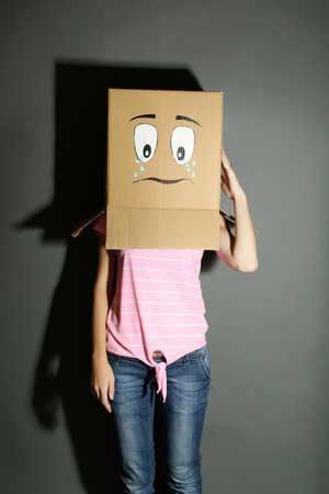 Woman with cardboard box on her head with sad face, on grey backgroundの写真素材