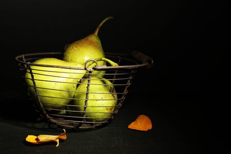 Ripe tasty pears in metal basket, on table, on dark backgroundの写真素材