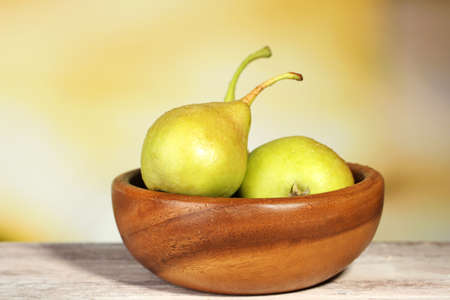 Ripe tasty pears in wooden bowl, on table, on nature backgroundの写真素材