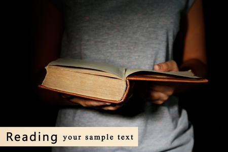 Woman holding very old book with dust, on dark backgroundの写真素材