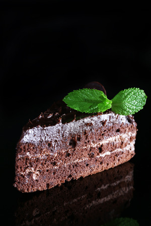 Piece of chocolate cake with mint leaves on glass table isolated on blackの写真素材
