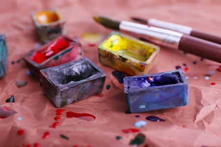 Watercolor paint cubes with brushes and spilled paint on brown paper background