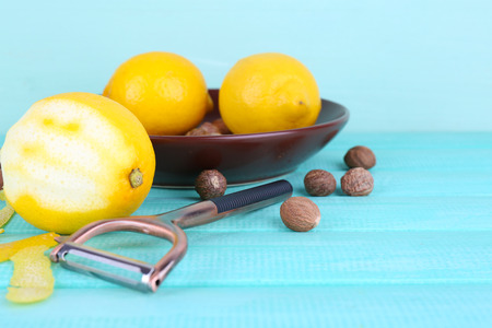Ripe lemons and nutmegs on plate and half peeled lemon with peeling knife on blue wooden backgroundの写真素材