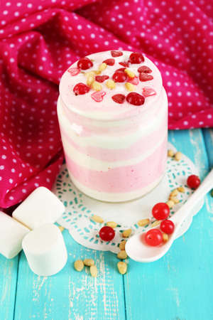 Raspberry milk dessert in glass jar, on color wooden background