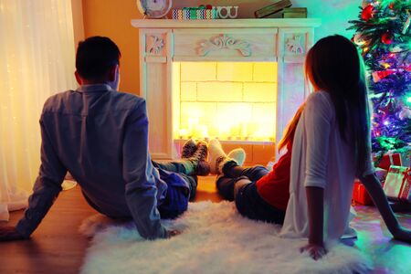 Nice love couple sitting on carpet in front of fireplace. Woman and man celebrating Christmasの写真素材