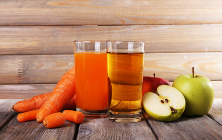Carrot and apple juice and fresh carrots and apples on wooden table on wooden wall backgroundの写真素材