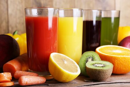 Fruit and vegetable juice in glasses and fresh fruits and vegetables on wooden table on wooden wall backgroundの写真素材